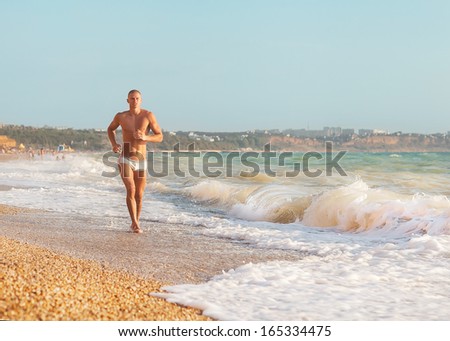 Running man jogging on beach. Male runner training outside working out. Fit young male sport fitness model exercising in full body in summer. Handsome strong caucasian man in his twenties.