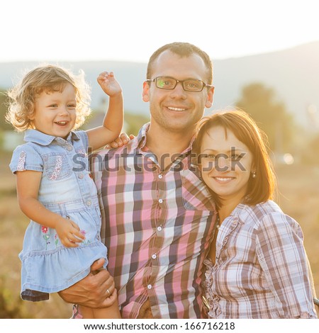 Happy mother, father and daughter in sunset