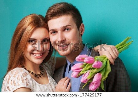 Portrait of young couple in love with flowers tulips posing at studio dressed in classic clothes