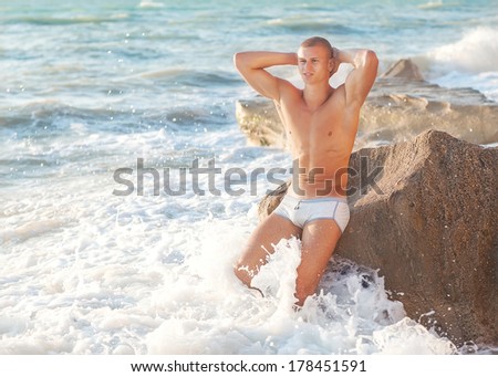 Fit worked-out man walking out of ocean onto beach with sky background and reflection in foreground