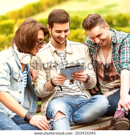 Three young men friends using tablet computer in park