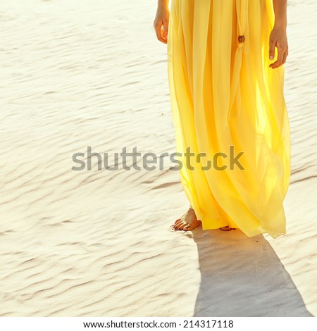 girl in a yellow dress walking barefoot on the white sand beach