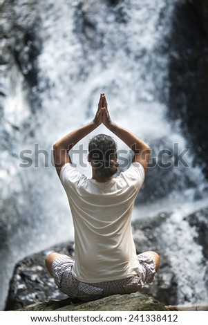 young man yoga engaged in the waterfall in the mountains yoga