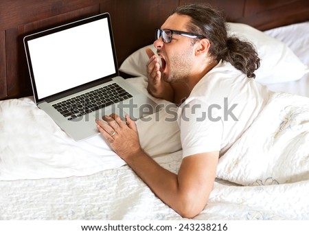 freelancer man with laptop yawns early in the morning in his bed, the work is free earnings, happy business