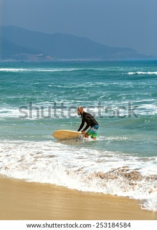 Surfer at the sea is standing with a surf board yellow color.