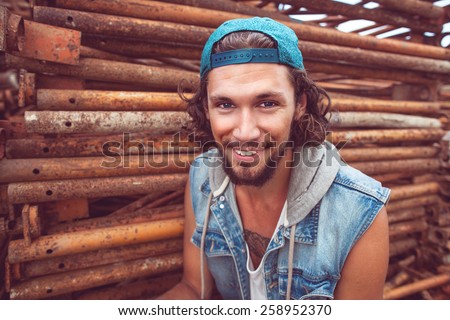 Portrait hipster fashion man dressed inÃ?Â  jeans jacket sitting on the iron frame begraund smiling