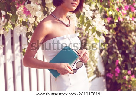fashion girl in white dress and turquoise bag standing near a white fence in the European fashion colors, concept Vogue