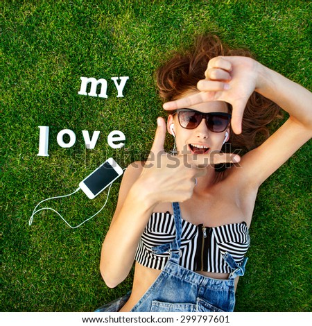 girl lying on the green grass, makes a stop frame arms, listening to music on a white label trave- My Love