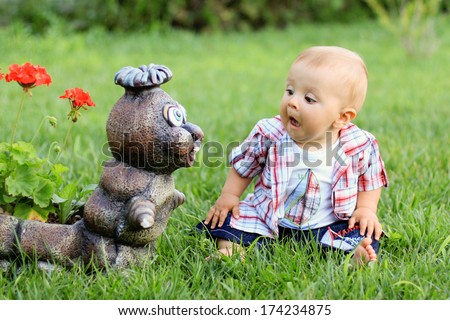 Little boy, making funny faces on a statue in a garden