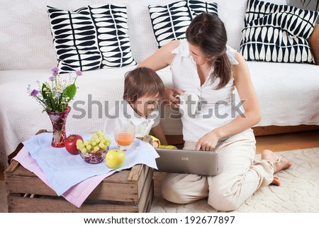 Mother and child, looking at a computer, eating fruits at cozy home