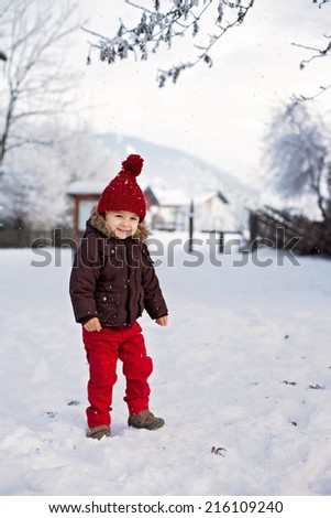 Portrait of child in brown jacket and red knitted hat and red trousers, lots of snow. Winter forest