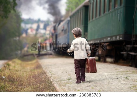 Boy, dressed in vintage shirt and hat, with suitcase, on a railway station, steam train