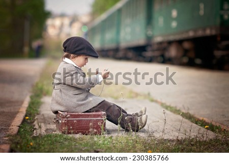 Boy, dressed in vintage coat and hat, with suitcase, on a railway station, steam train