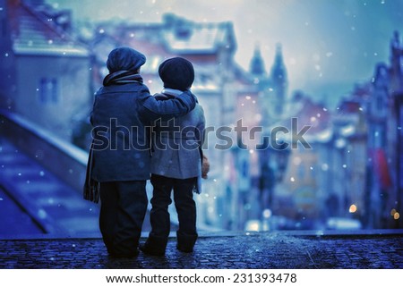 Silhouettes of two kids, standing on a stairs, backwards, view of Prague behind them, snowy evening