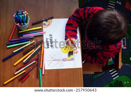 Adorable little boy, drawing picture for easter at home, having fun, smiling at camera, shot from above