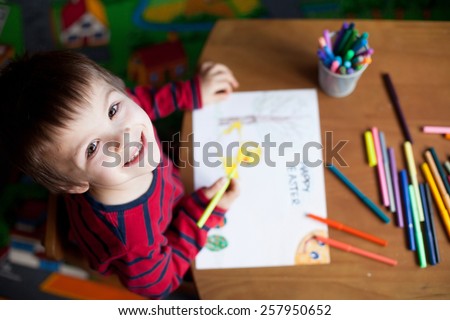 Adorable little boy, drawing picture for easter at home, having fun, smiling at camera, shot from above