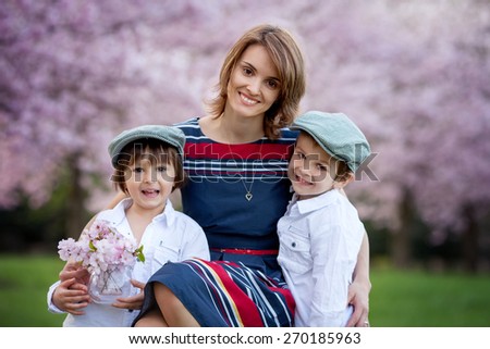 Beautiful kids and mom in cherry blossom spring park, child giving flowers to mother. Mothers day celebration concept