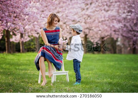 Beautiful kid and mom in cherry blossom spring park, child giving flowers to mother. Mothers day celebration concept