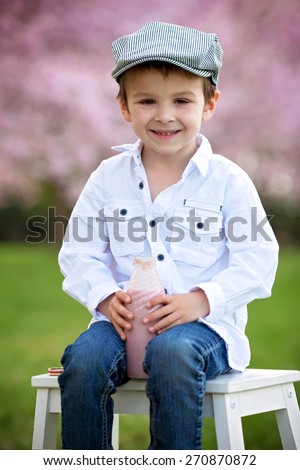 Close portrait of adorable little caucasian boy in a cherry tree blooming garden in the afternoon, drinking smoothie