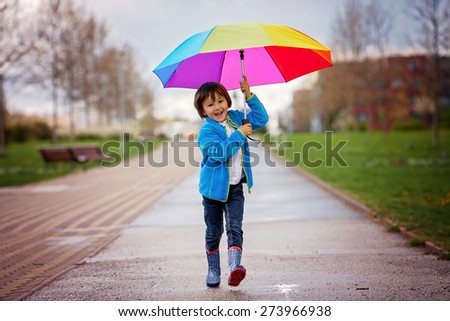 Cute little boy, walking in a park on a rainy day, playing and jumping, smiling, springtime