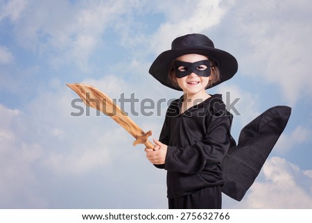 Superhero child with a sword against blue sky background, smiling at the camera, black clothing and a mask