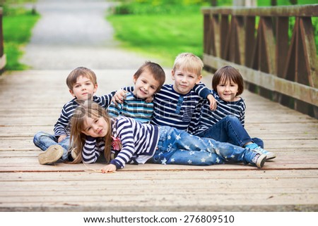 Five adorable kids, dressed in striped shirts, hugging and smiling, little girl lying on the ground, four boys behind her