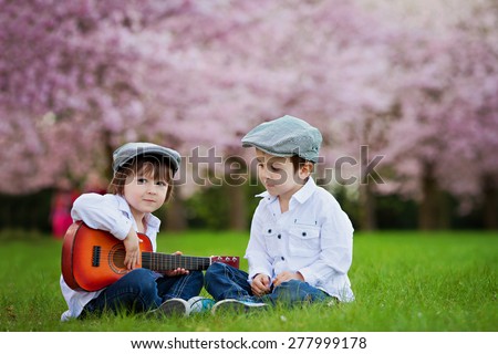 Two adorable caucasian boys in a blooming cherry tree garden, playing guitar in the afternoon