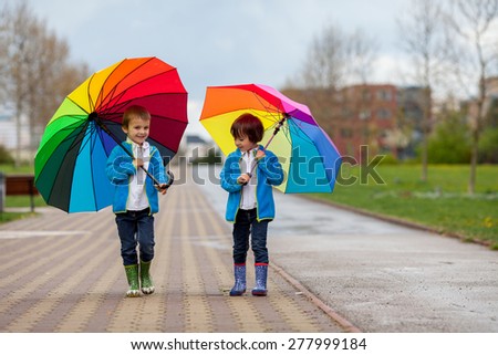 Two adorable little boys, walking in a park on a rainy day, playing and jumping, smiling, talking together, springtime