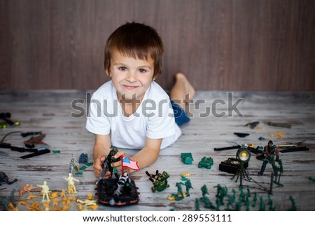 Cute little toddler boy, playing at home with soldiers and figurine toys, playing wars and peace