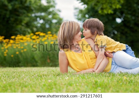Young beautiful mom and her cute little boy, relaxing and having fun in the park, spring afternoon, yellow clothing