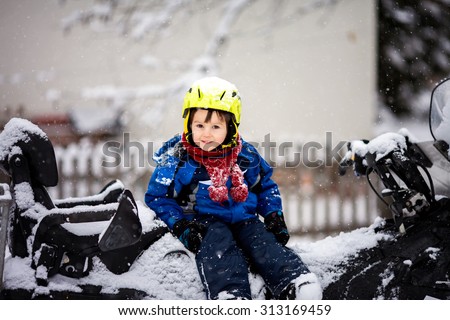 Happy little kid is playing in snow, good winter weather, ski gear, sitting on a snow motor sledge