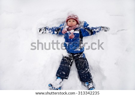 Adorable little boy in blue jacket, red hat and scarf,  lying on north pole snow, making snow angel