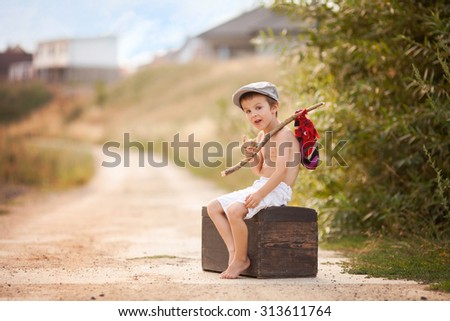 Cute little boy, sitting on a big old suitcase, vintage, holding a bundle, eating bread and smiling