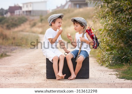 Two boys, sitting on a big old vintage suitcase, eating marshmallows and talking
