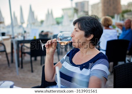 Middle aged woman, drinking rose wine in a beach restaurant, enjoying a warm evening