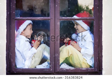 Two cute boys, brothers looking through a window, holding cups with tea, waiting for Santa