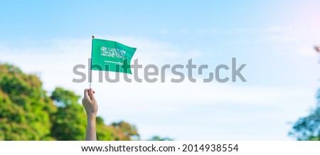 hand holding Saudi Arabia flag on blue sky background. September Saudi Arabia national day and Happy celebration concepts