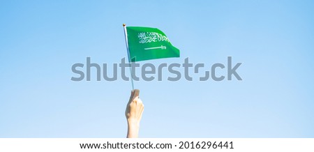 hand holding Saudi Arabia flag on blue sky background. September Saudi Arabia national day and Happy celebration concepts