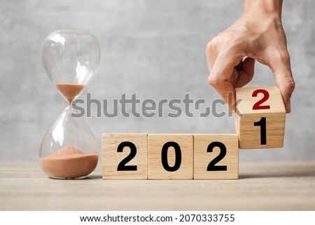 hand flipping block 2021 to 2022 text with hourglass on table. Resolution, time, plan, goal, motivation, reboot, countdown  and New Year holiday concepts
