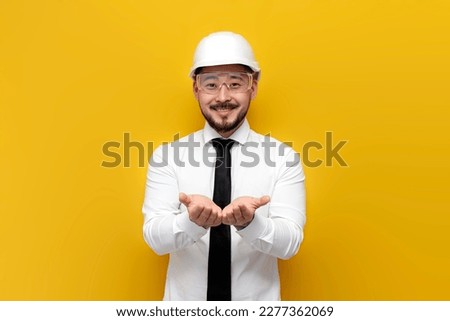 asian foreman in shirt with tie holds blank space with his hands on yellow isolated background, korean civil engineer in formal wear holds his hands in front of him ストックフォト © 