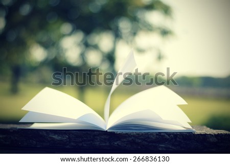 open book with flying book page on wood table (vintage background)