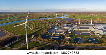 Wind turbines, water treatment and bio energy facility and solar panels in The Netherlands part of sustainable industry in Dutch flat river landscape against blue sky. Aerial circular economy concept.