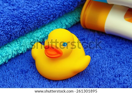 Yellow rubber duck in the background of two blue Terry  towels and two white plastic bottles with yellow and blue cover, closeup