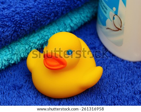 Yellow rubber duck in the background of two blue Terry towels and one white plastic bottle with a blue label