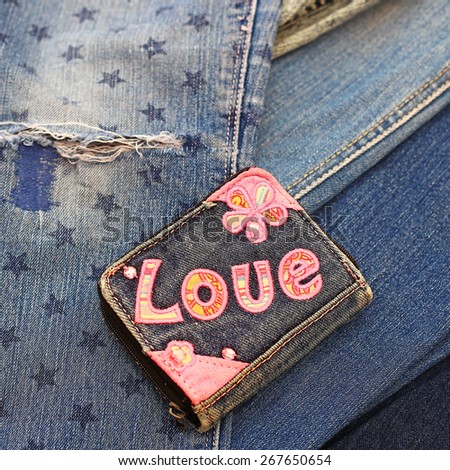 Shabby blue denim purse with embroidered pink word LOVE and flowers on the destroyed torn denim blue jeans background