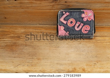 Shabby torn denim blue purse with embroidered pink word LOVE and flowers on rustic wooden background, the focus is not centered,  on the word  LOVE
