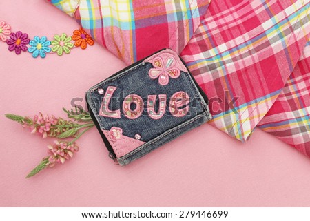 Shabby torn denim blue purse with embroidered pink word LOVE and flowers on plaid skirt and a pink T-shirt with embroidered multicolored flowers background