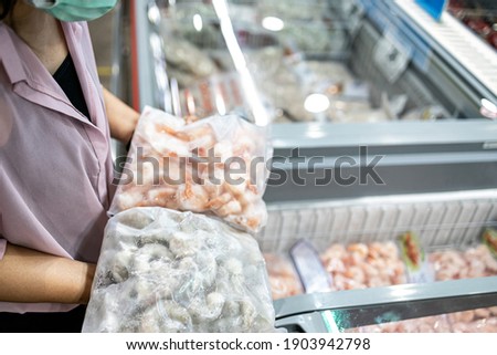 Asian woman choosing frozen food products,compare the dissimilarity between fresh shrimp and frozen raw shrimp,buy the necessary food,hoard packed frozen seafood at freezer,shopping in the supermarket