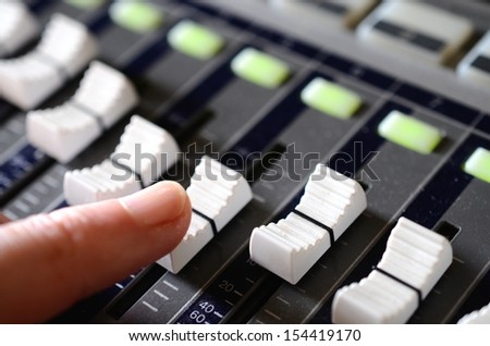 Finger pushing a fader on a sound mixing desk in a recording studio.