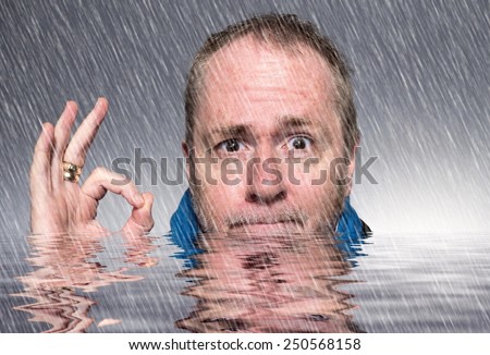 Positive thinking - man up to his neck in flood water but still smiling and giving the ok sign.